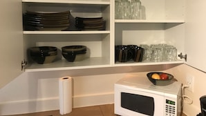 A kitchen with white cabinets, a microwave, and various kitchenware including bowls, plates, and cups.