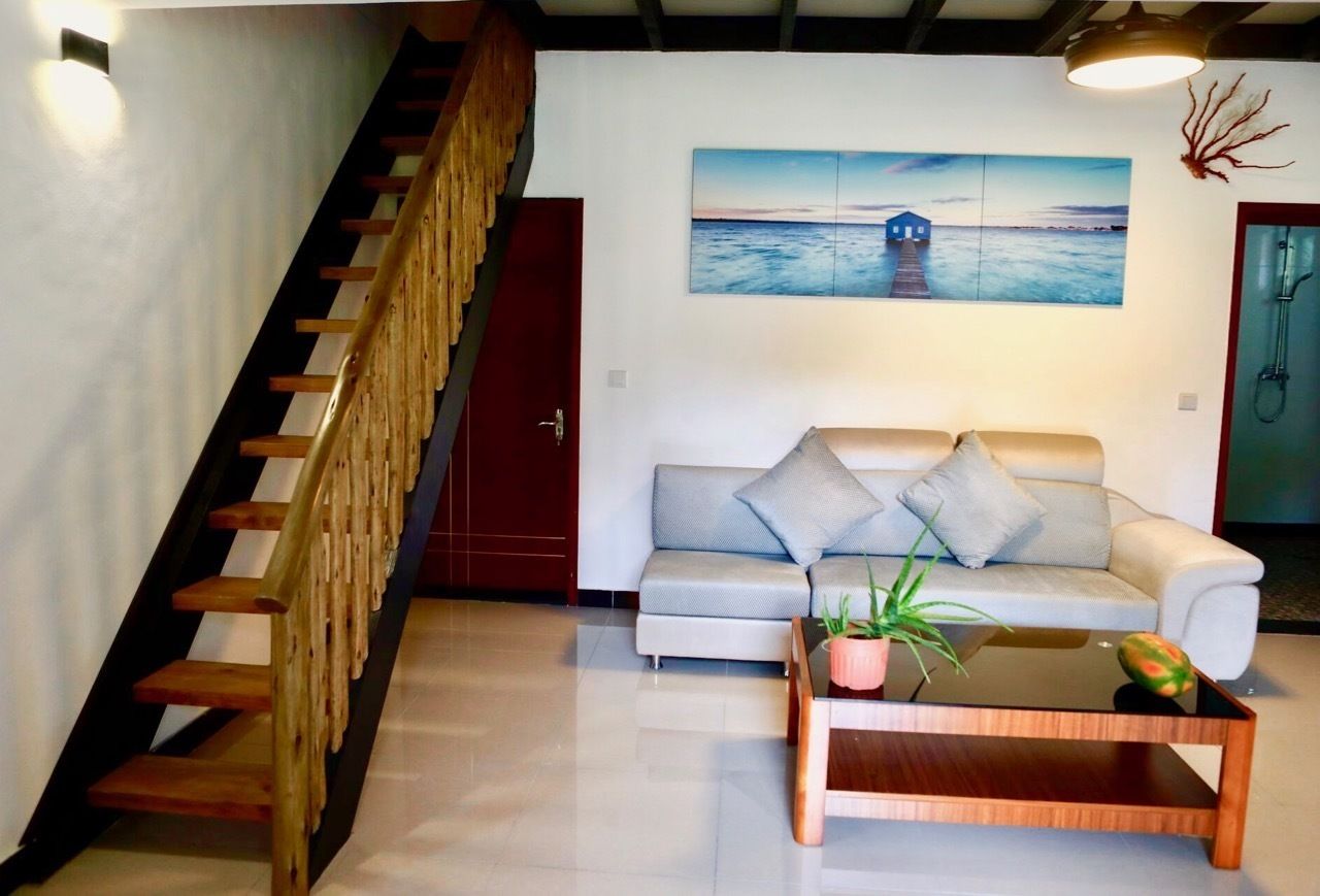 Una sala de estar con una escalera, un sofá, una mesa de centro y un cuadro de una escena costera.