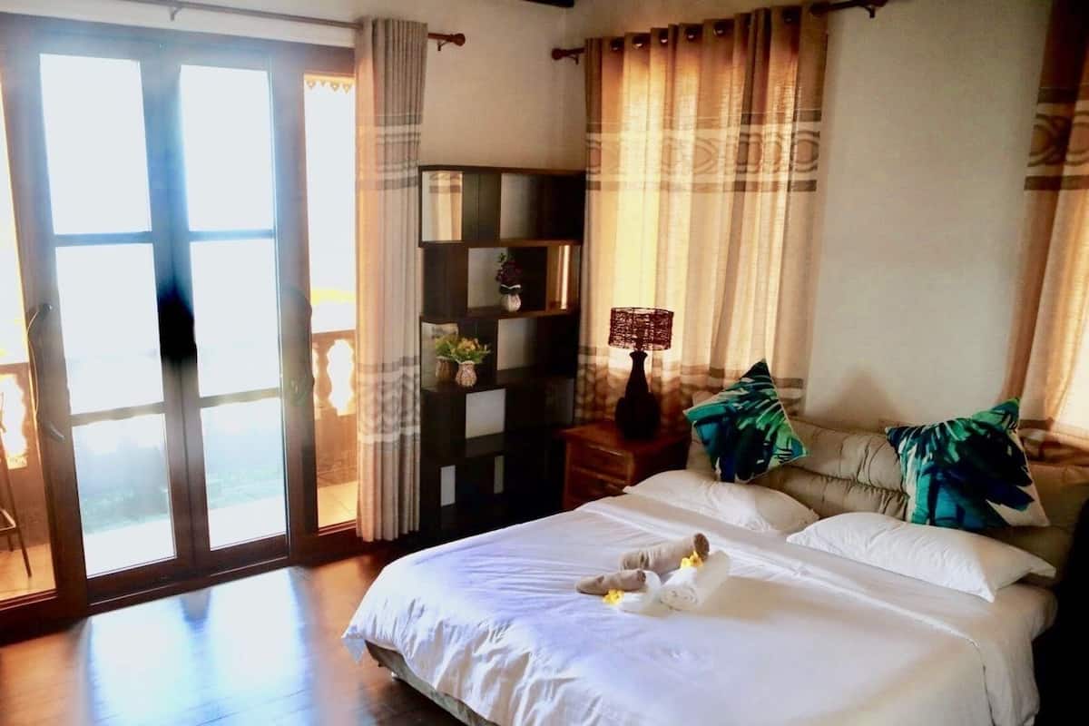 A bedroom with a large bed, a nightstand, a shelf with decorative items, and a view through the glass doors.