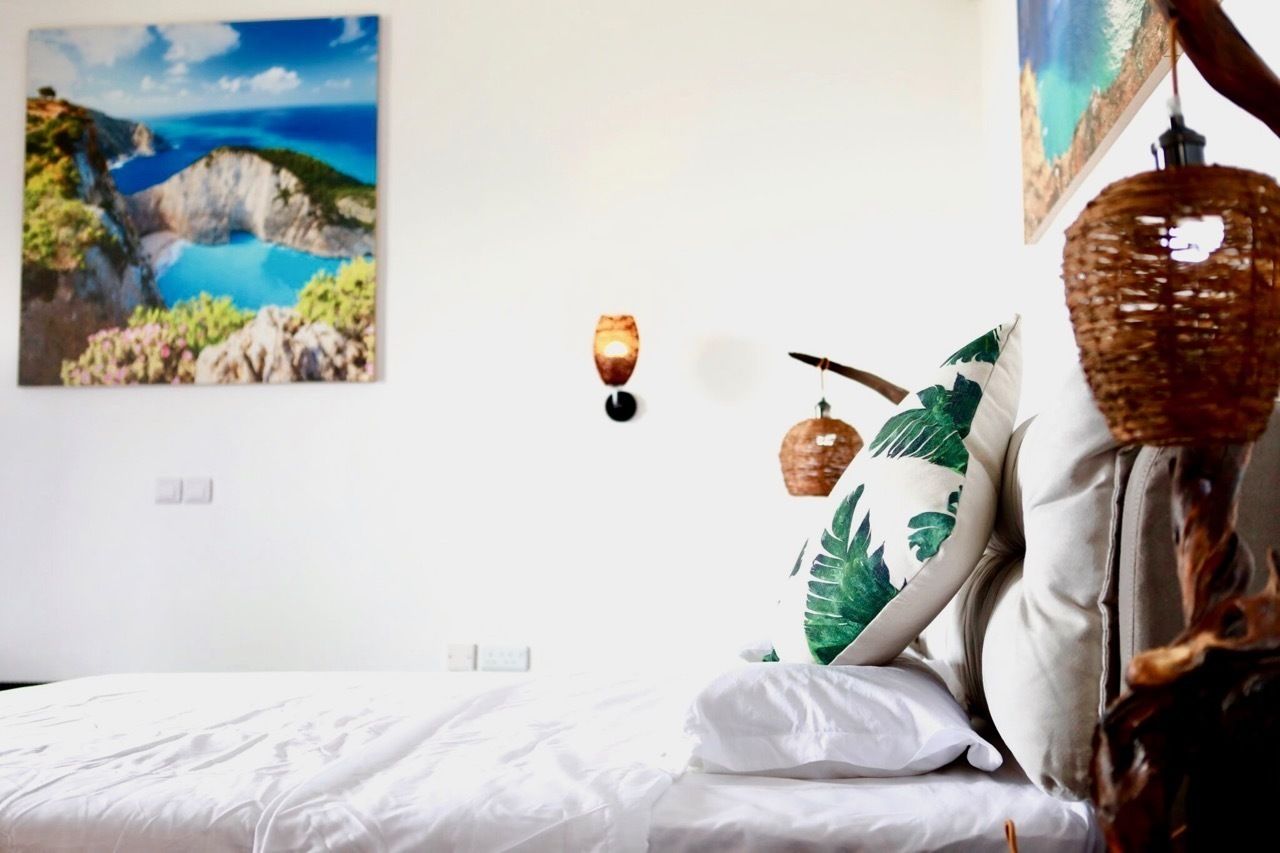 A bedroom with a bed, a wall-mounted light, and a painting of a coastal landscape.