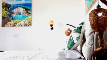 A bedroom with a bed, a wall-mounted light, and a painting of a coastal landscape.