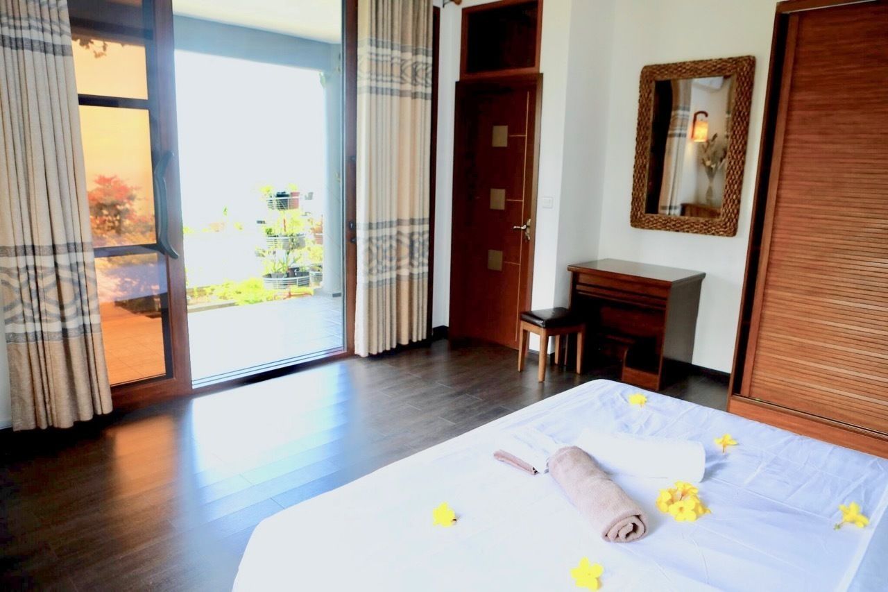 A hotel room with a bed, a desk, a chair, a wardrobe, and a sliding glass door leading to a balcony.