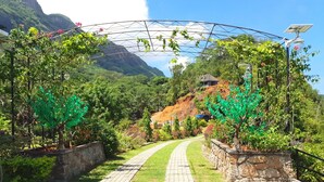 A paved pathway leading through a landscaped area with trees and a mountain backdrop. - Blue Hill (Mahé Island)