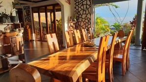 A spacious dining area with a long wooden table and chairs, surrounded by potted plants and a view of the outdoors. - Blue Hill (Mahé Island)