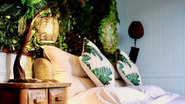 A bedroom with a bed, wooden nightstand, and a hanging plant. - Blue Hill (Mahé Island)