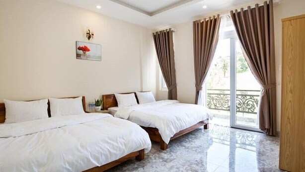 A hotel room with two beds, a wooden door, a balcony with curtains, and a framed picture on the wall. - Huong Anh Luxury Hotel Dalat (Lang Biang - Da Lat)