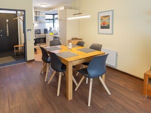 A dining area with a wooden table and chairs, a kitchen in the background, and a framed picture on the wall. - Vacation home Marisol, holiday apartment rental North Sea - Holiday home Marisol (Varel)