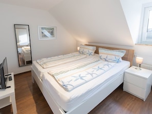 A bedroom with a large bed, a bedside table with a lamp, a mirror, and a framed picture on the wall. - Vacation home Marisol, holiday apartment rental North Sea - Holiday home Marisol (Varel)