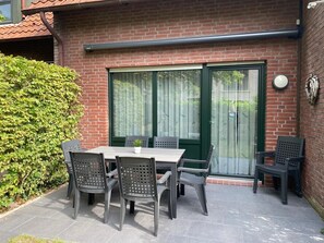 A patio with a table and chairs, a green door, and a brick wall. - Vacation home Marisol, holiday apartment rental North Sea - Holiday home Marisol (Varel)