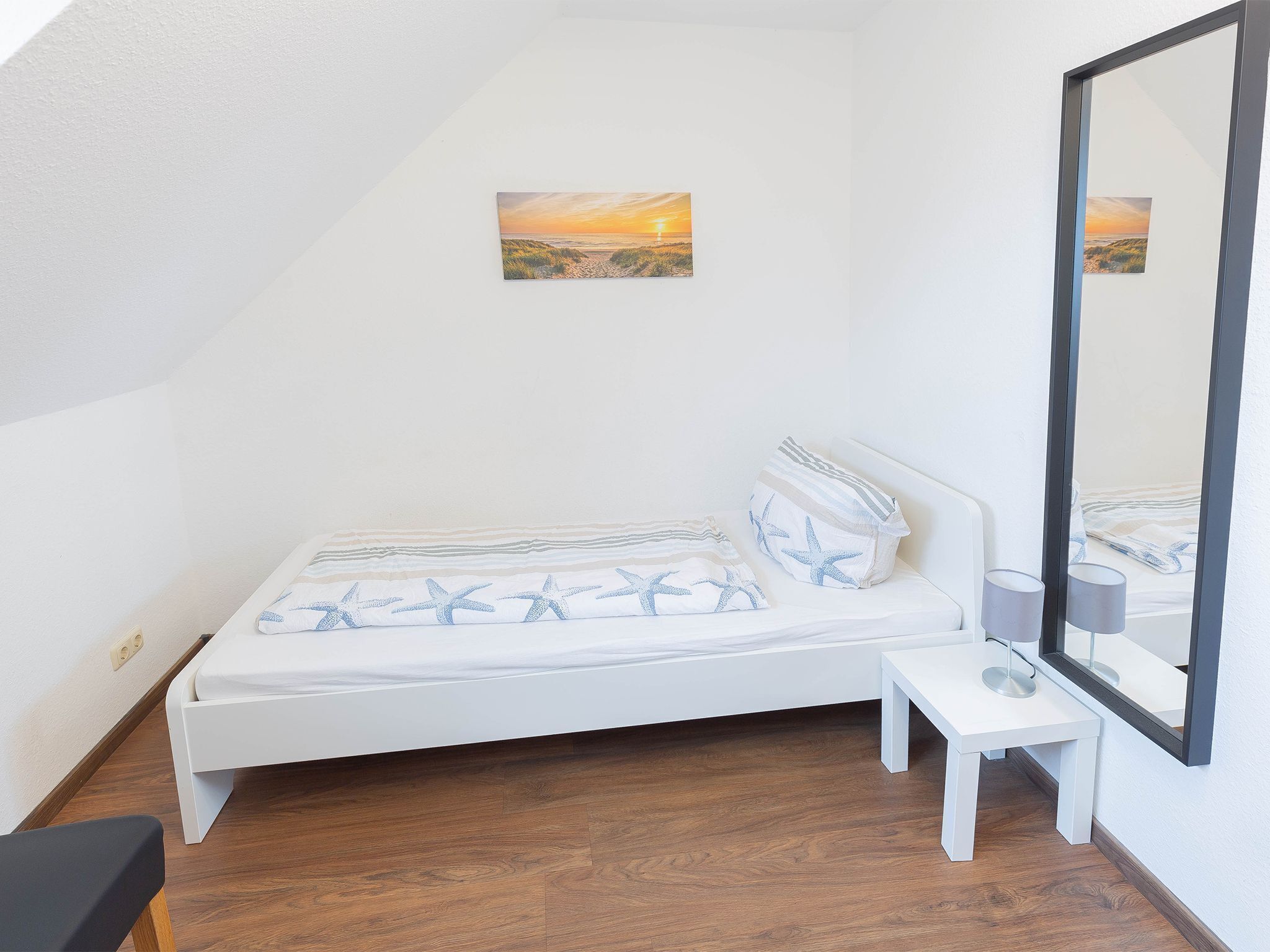 Ein Schlafzimmer mit Bett, Nachttisch, Lampe und einem großen Spiegel.