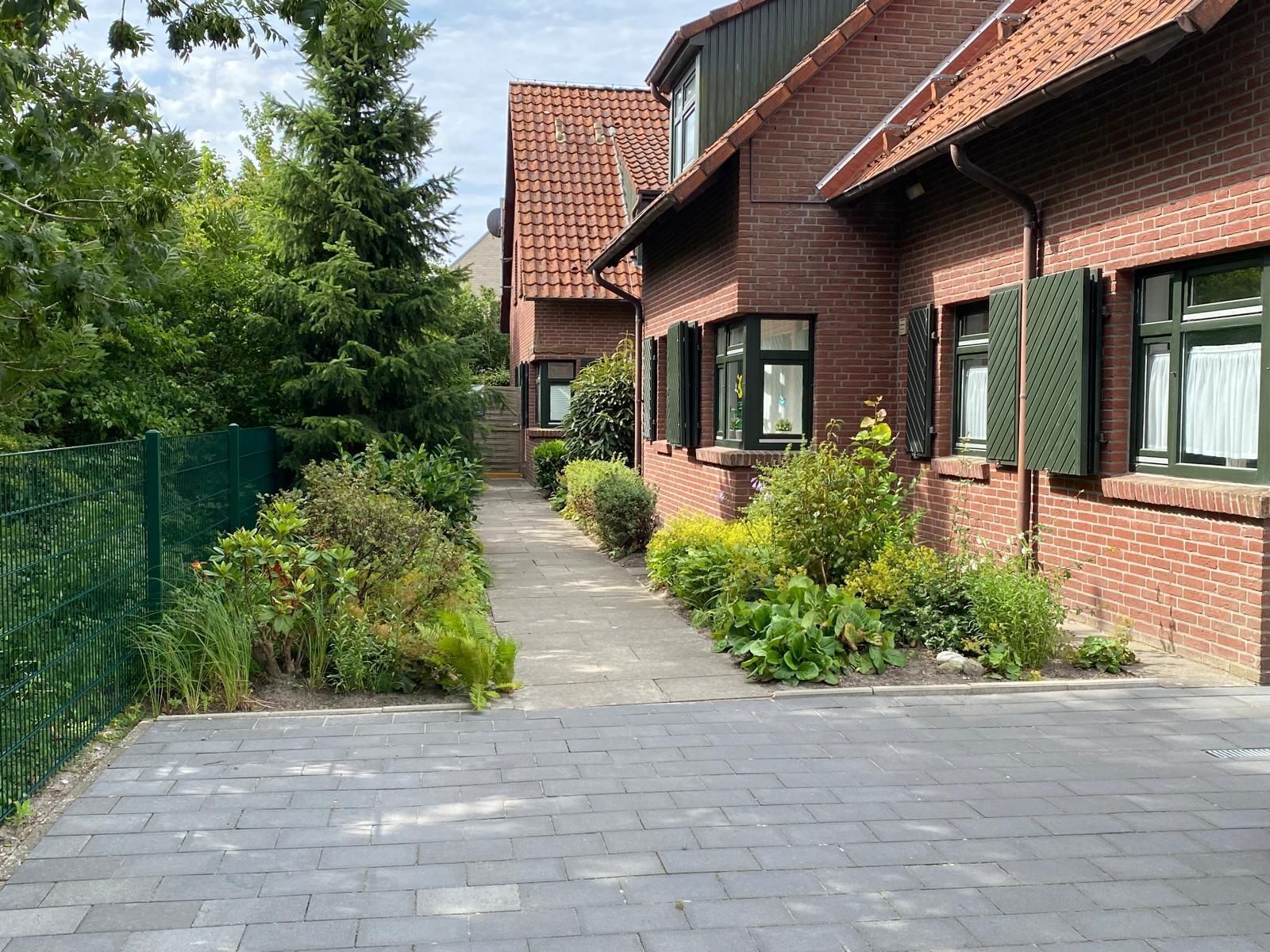 A residential building with a brick facade, green shutters, and a paved pathway leading to the entrance.