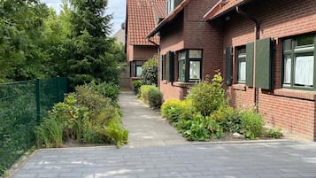 A residential building with a brick facade, green shutters, and a paved pathway leading to the entrance.