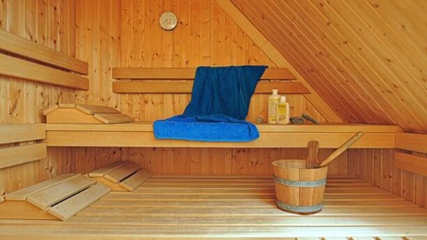 A wooden sauna with benches, a blue towel, a wooden bucket, and a bottle of lotion. - House Pier 18 - Holiday apartment 9 (Esens)