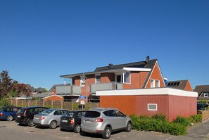 A parking lot with several cars and a building with a red facade and white trim. - House Pier 18 - Holiday apartment 9 (Esens)