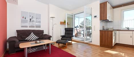 Een moderne woonkamer met een bank, een salontafel, een rode vloerkleden, een zwarte stoel, en een keuken met houten kasten en een raam.