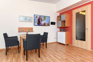 Uma sala de estar moderna com área de jantar, televisão na parede e um armário de madeira com portas de vidro.