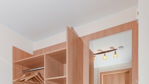 A walk-in closet with open shelving, a hanging rod, and a small wooden stool. - House Pier 18 - Holiday apartment 9 (Esens)
