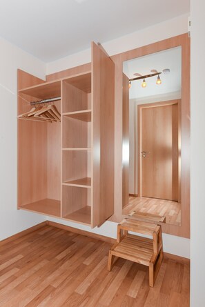 Un dressing accessible sans porte, doté d’étagères ouvertes, d’une tringle à vêtements et d’un petit tabouret en bois.