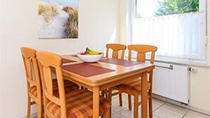 Un coin repas avec une table en bois et quatre chaises, un saladier rempli de fruits et une fenêtre donnant sur un paysage verdoyant.