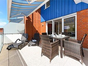 En udendørs terrasse med fletmøbler, et spisebord og en blå markise, der giver skygge.