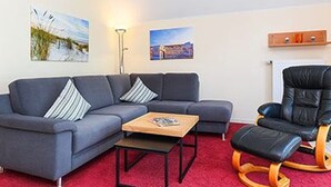 Un salon avec un canapé gris, un fauteuil en cuir noir, une table basse en bois et un tapis rouge.