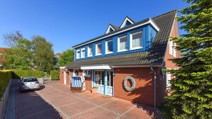 Une maison à deux étages, à la façade bleue et blanche, avec une allée pavée et une voiture garée dans l’allée.