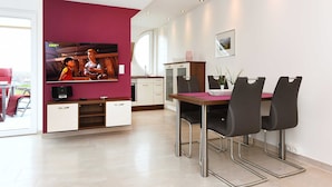 Un espace de repas moderne avec un téléviseur, une table à manger, des chaises et une cuisine en arrière-plan.