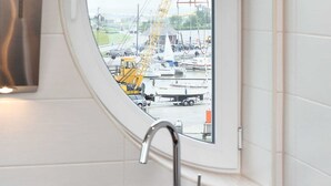 Une cuisine dotée d’une fenêtre ronde donnant sur un port de plaisance et sur des grues de chantier.