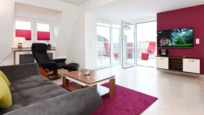 Un salon moderne avec un canapé gris, une table basse en bois et un téléviseur fixé sur un mur rouge.