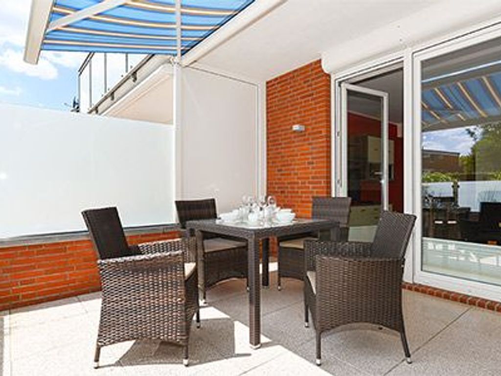 A patio with wicker furniture and a table set for two, a glass door leading inside, and a clear view of the outside.