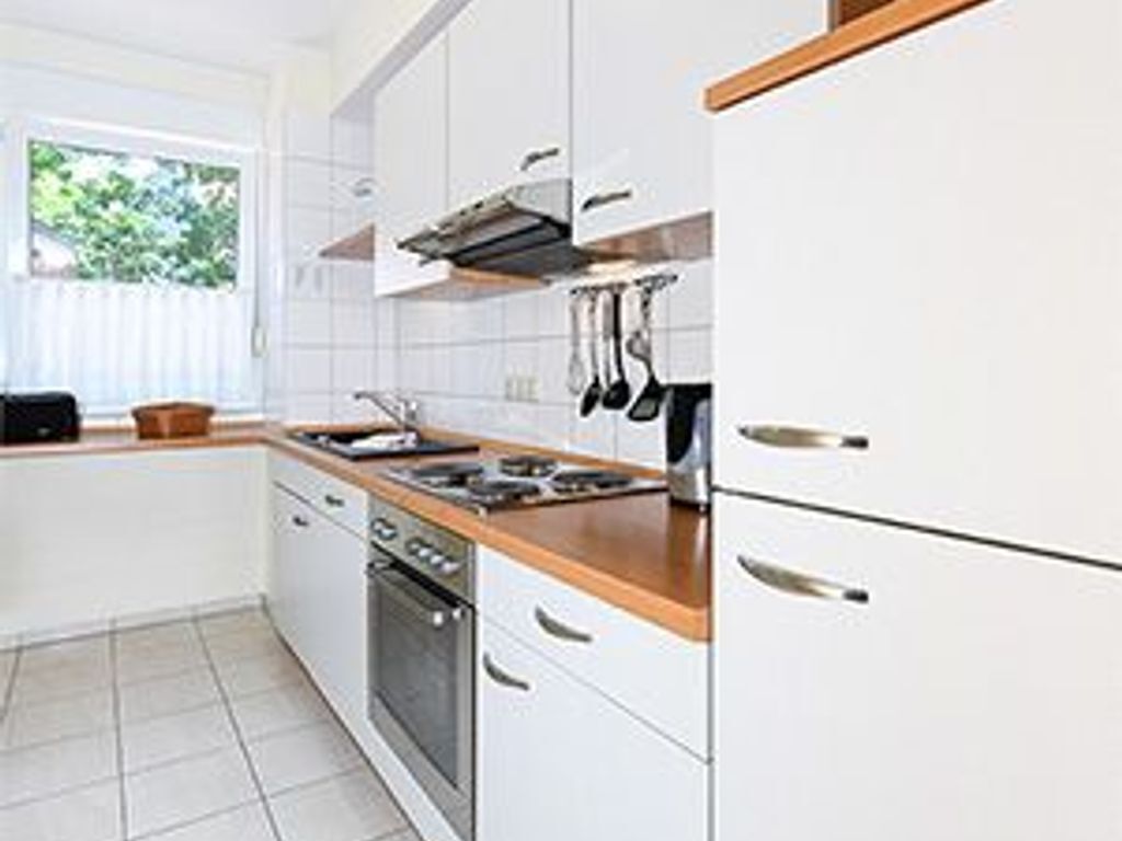Una cocina moderna con armarios blancos, encimera de madera y electrodomésticos de acero inoxidable.