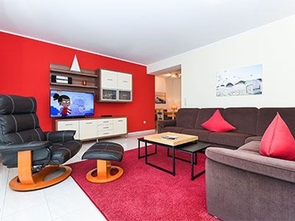 Un salon moderne avec un mur d’accent rouge, un canapé en cuir, un fauteuil en cuir noir, une table basse et un téléviseur.