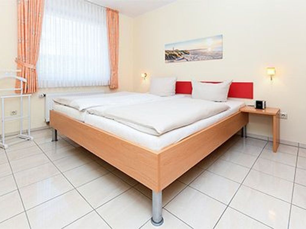 A modern hotel room with a large bed, a bedside table, a nightstand, and a window with curtains.