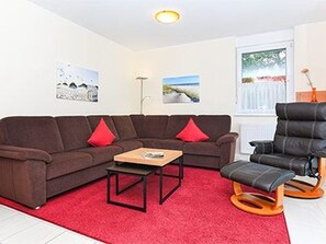 A living room with a sectional sofa, a small table, a recliner, and a red carpet.