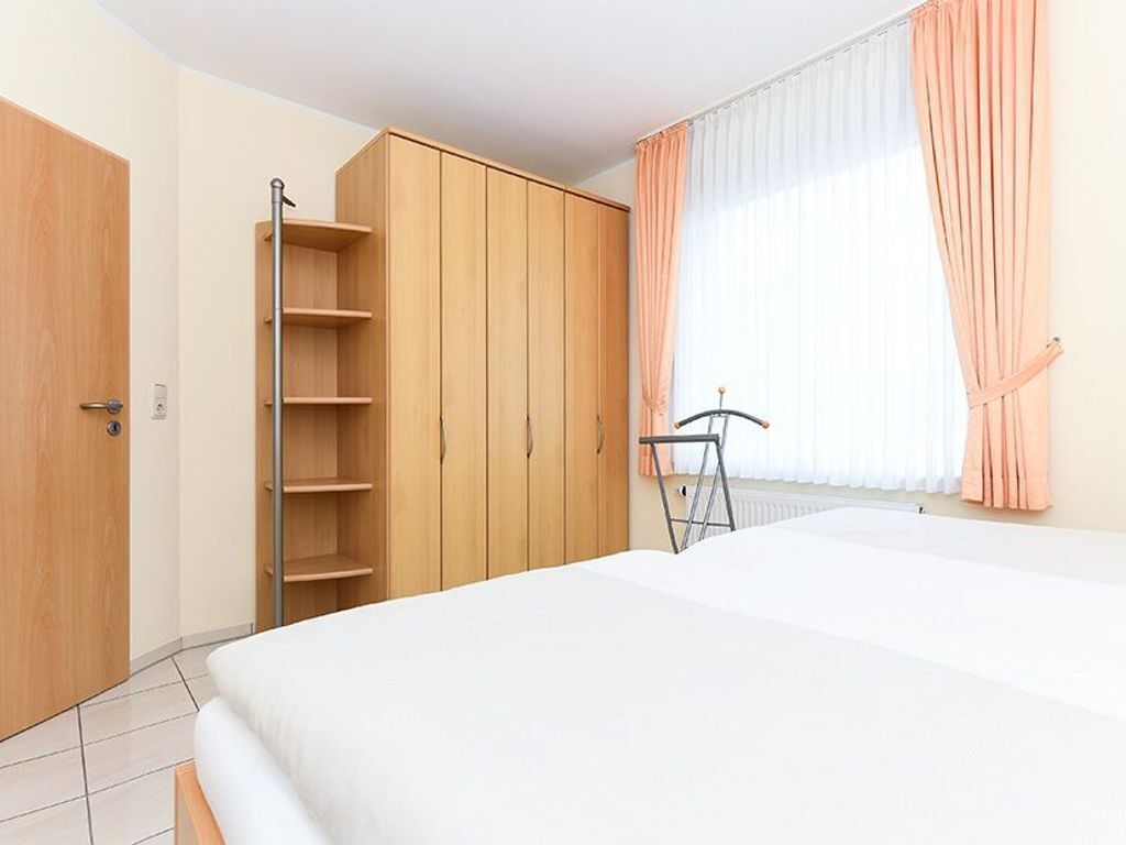 Un dormitori amb un llit, un armari de fusta i una finestra amb cortines.