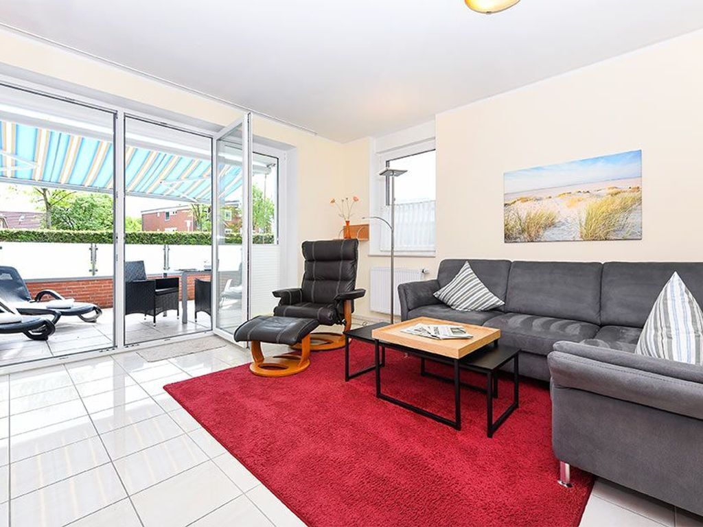 Un salon moderne avec un canapé gris, un tapis rouge et une porte vitrée donnant sur un espace extérieur.