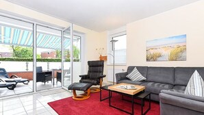 Ett modernt vardagsrum med en grå soffa, en röd matta och en glasdörr som leder ut till ett utomhusområde.
