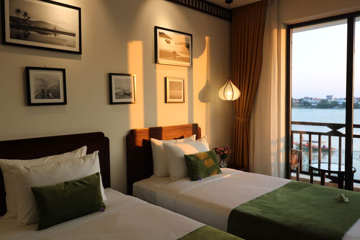 A hotel room with two beds, a large window with a view of the water, and framed pictures on the wall.