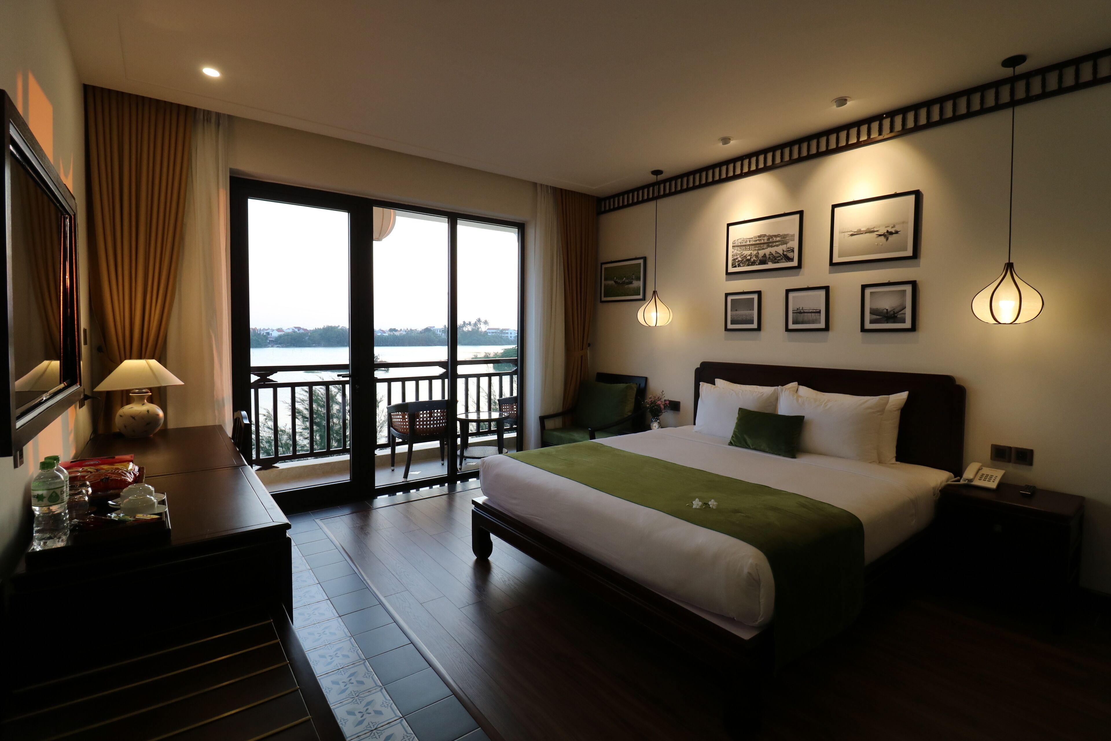 Una camera d'hotel con un letto grande, una scrivania con una lampada, un telefono e quadri appesi alle pareti.