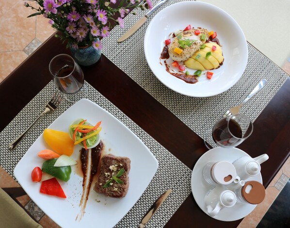 A dining table with two plates of food, a vase of flowers, and a set of cutlery.