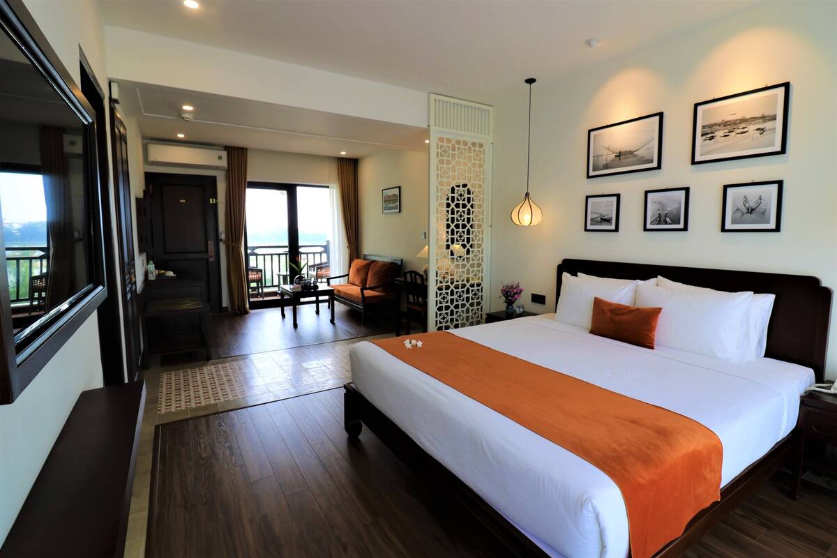 A hotel room with a large bed, a desk, a chair, and a view of the sea.