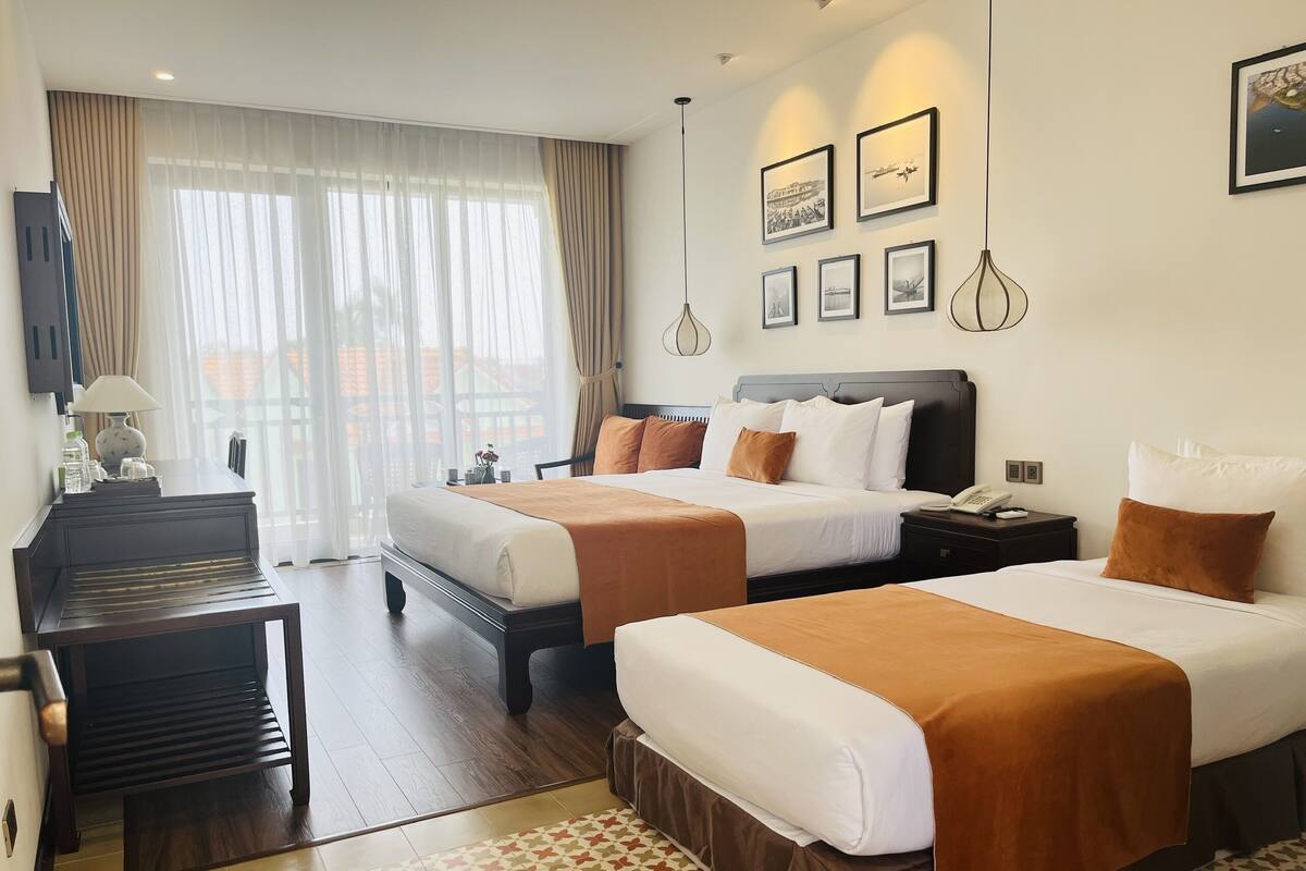 A hotel room with two beds, a desk, a chair, and a large window with curtains.