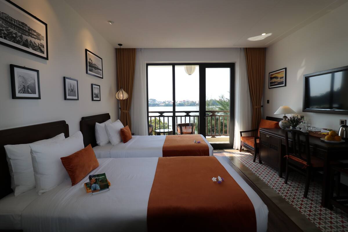 A hotel room with two beds, a dining area, a TV, and a balcony with a view.