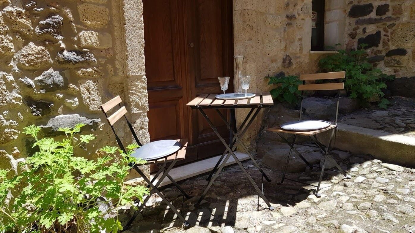 An outdoor seating area with a stone wall, a wooden door, and a small table with chairs.