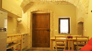A compact kitchen with a wooden door, a window with a curtain, and a dining area with chairs and a table.