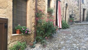 A narrow cobblestone street with stone buildings, potted plants, and a red and white striped curtain.