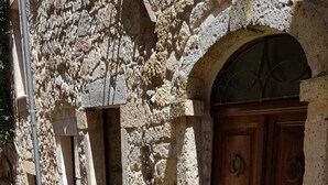 A stone building with a wooden door, a small table with chairs, and potted plants.