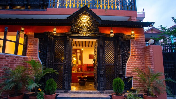 Un edificio tradicional con puertas negras ornamentadas, fachada de ladrillo rojo y plantas en macetas al frente.
