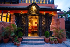 A traditional building with ornate black doors, a red brick facade, and potted plants in front.