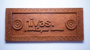 Un letrero de madera con el texto "nivas boutique home" rodeado de motivos florales decorativos.